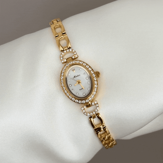 Leuchtend, schick, elegant: Uhr mit ovalem Zifferblatt aus weißem Perlmutt, diamantbesetzter Goldlünette und Edelstahlarmband.